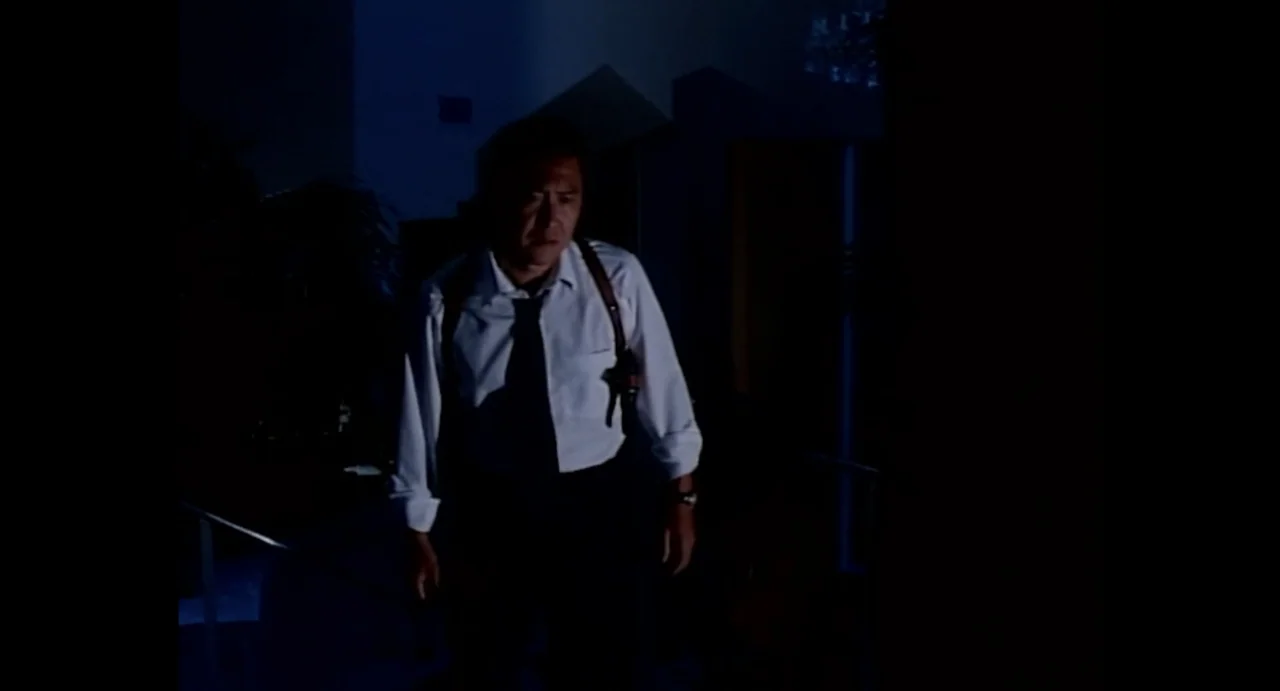 American Yakuza (1993) movie still: medium — An interior hallway features dark walls and a dimly lit path in an office building. A man in a white…