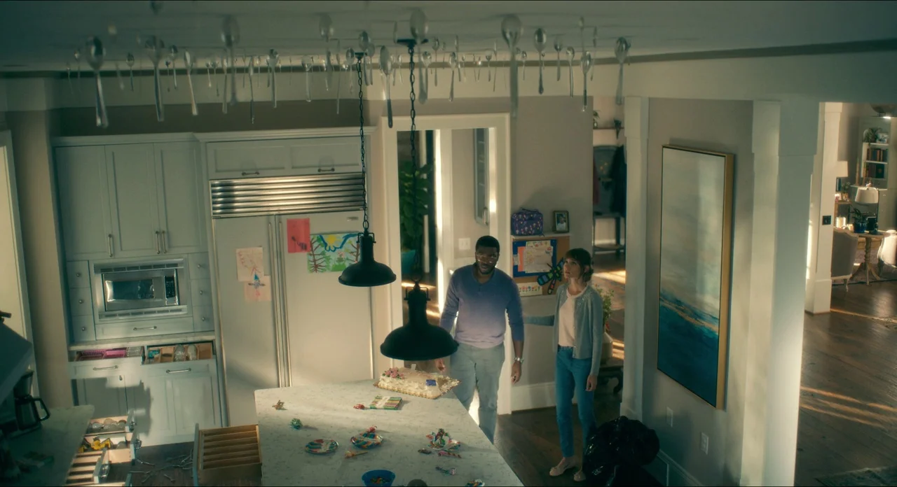 Doctor Sleep movie still: wide — An open plan domestic space featuring light-colored cabinetry and a central stone island. Dozens of silver spoons…
