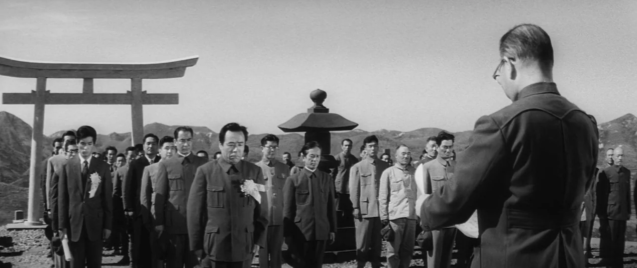 The Human Condition I: No Greater Love (1959) movie still: wide — An outdoor gathering stands in front of a stone torii gate and pagoda. A man…