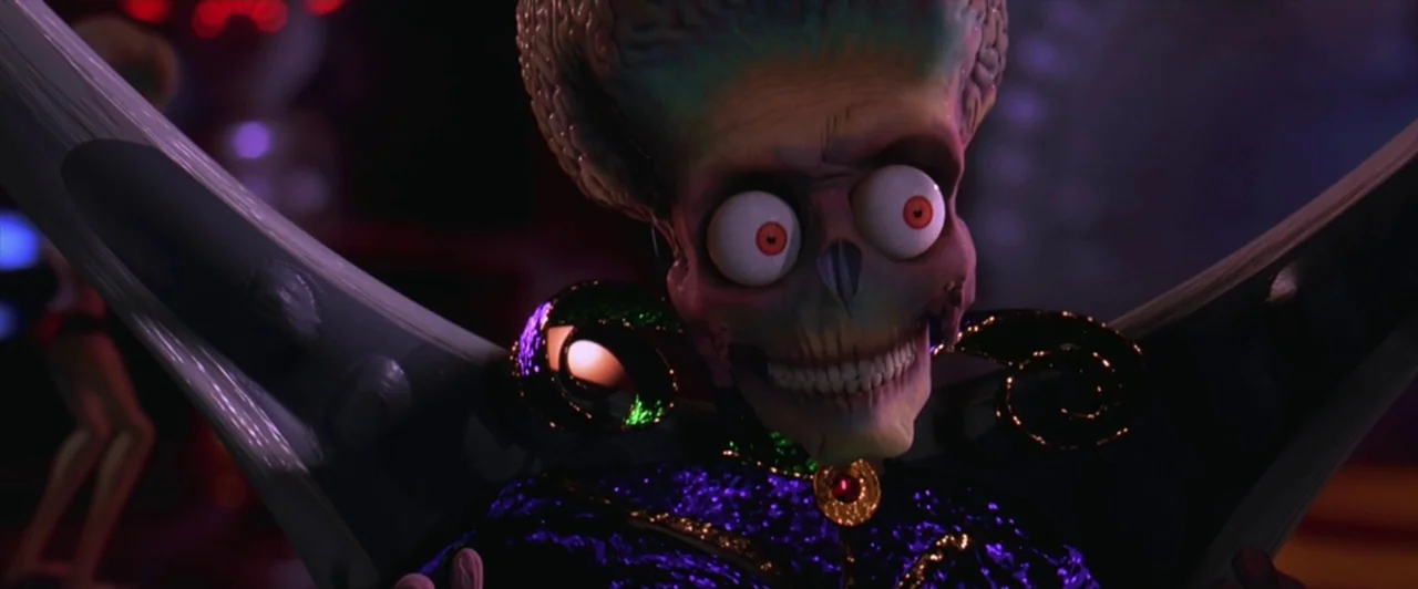 Mars Attacks! (1996) movie still: closeup — A dimly lit interior space with a dark, textured metallic structure surrounding the alien. The creature…