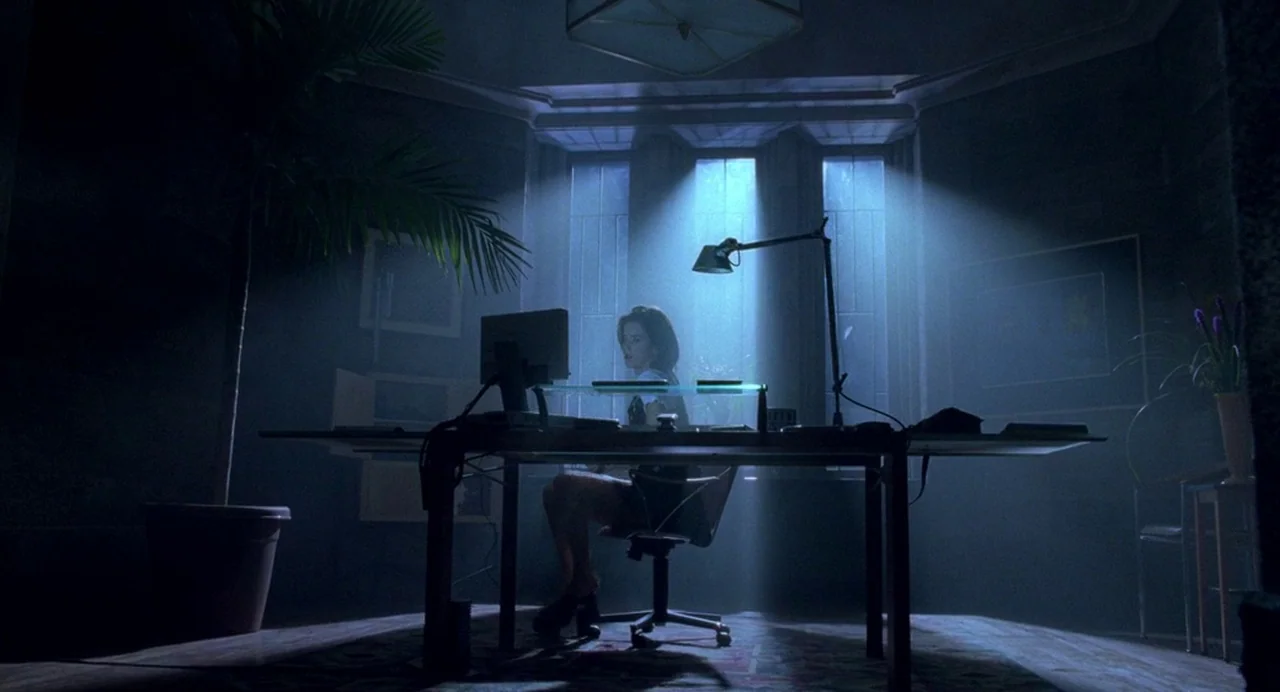 Bad Boys (1995) movie still: wide — A dimly lit room features a large desk positioned before a tall window. A woman sits on a swivel chair, looking…