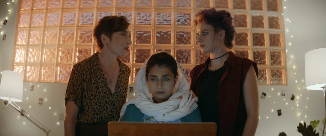 Mennonite's Bite (2023) movie still: medium — A contemporary living room featuring a back-lit glass block wall with decorative string lights. Three…