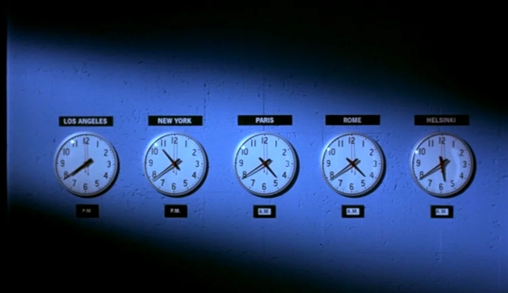 Night on Earth (1991) movie still: medium — A dark wall features five side-by-side analog clocks labeled with major international city names. Each…