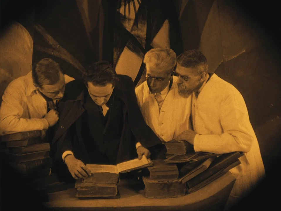 The Cabinet of Dr. Caligari (1920) movie still: medium — An interior study with abstract painted backdrops features a cluster of old stacked books.…