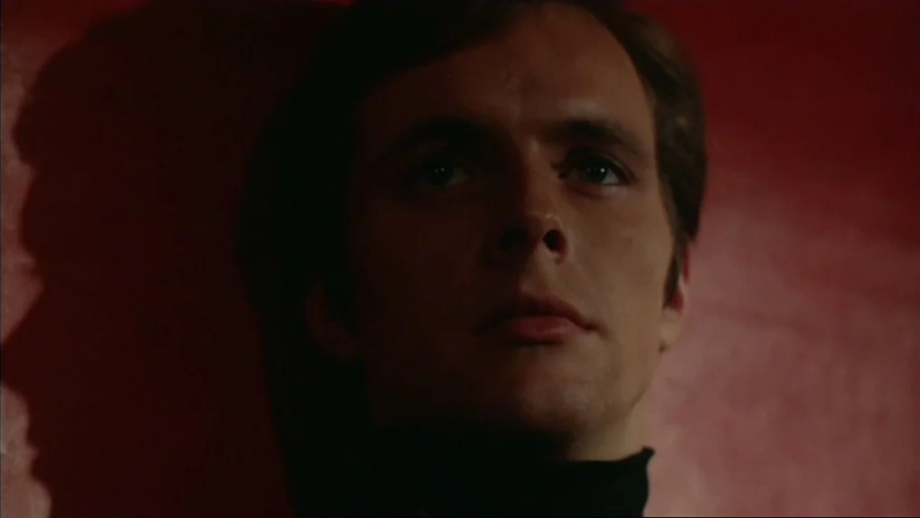 The Sorcerers (1967) movie still: closeup — A man stands against a stark red wall in a dim setting. The subject gazes towards the right side of the…