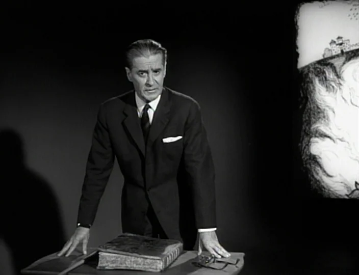 The Devil’s Eye (1960) movie still: medium — A man stands in a dark studio set against a blank backdrop. He is positioned behind a desk with a large…