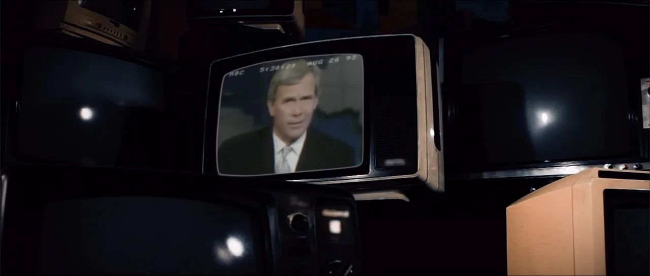 Square One (2019) movie still: medium — A pile of vintage CRT television sets are stacked in a dark space. The central screen displays a man in a…