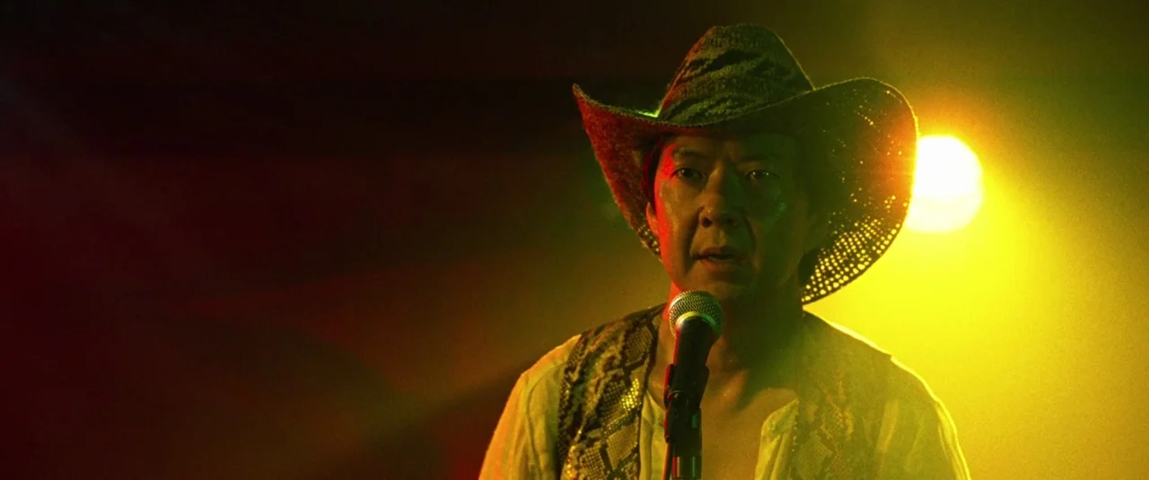 The Hangover Part III (2013) movie still: medium — A man stands on a stage bathed in intense yellow and red spotlights. He holds a microphone close…