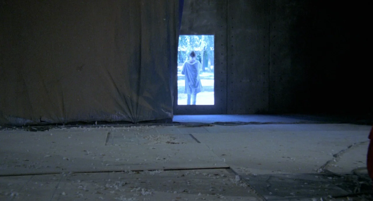 StageFright (1987) movie still: wide — A dark, unfinished construction space with concrete walls and scattered debris on the floor. A woman stands…