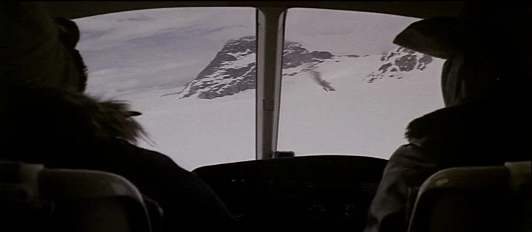 The Thing (1982) movie still: medium — The interior of a helicopter cockpit shows two people from behind looking forward. A large expanse of…