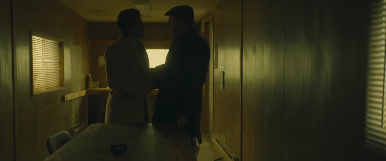A Most Violent Year (2014) movie still: medium — A cramped construction trailer features wood-paneled walls and slatted blinds over small windows.…