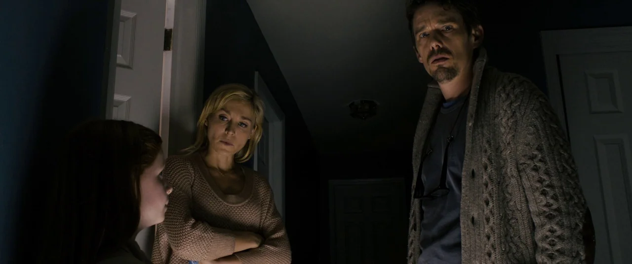 Sinister (2012) movie still: medium — A dark, dimly lit domestic hallway with deep blue walls and white door frames. Two adults and a child stand in…