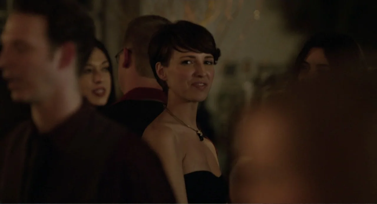 Before We Go (2014) movie still: medium — An interior space filled with people at a dimly lit social event. A woman in a black strapless dress looks…