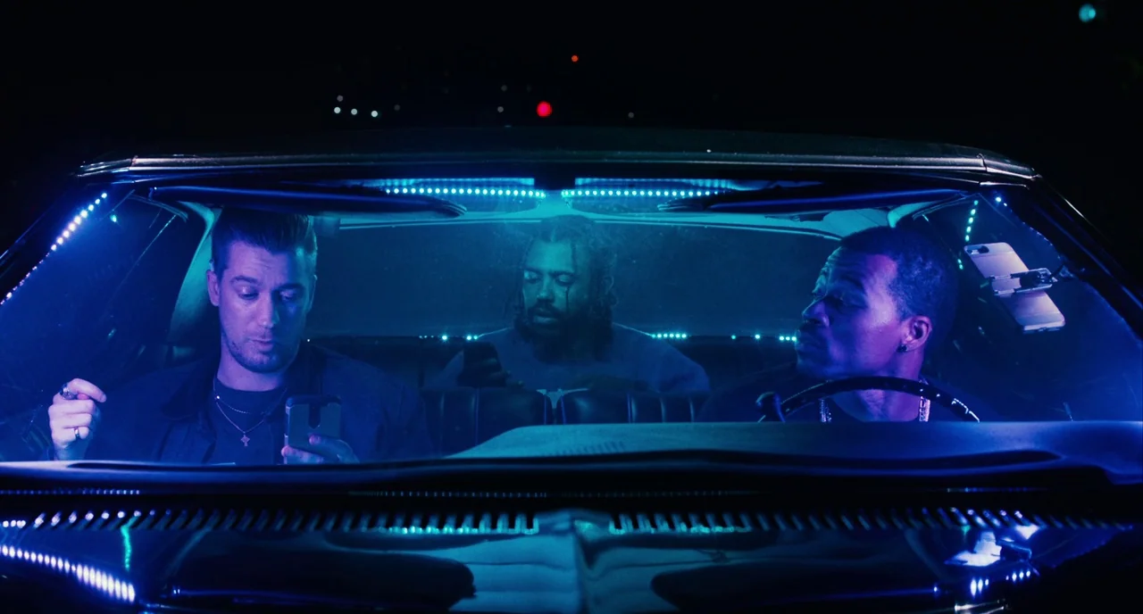Blindspotting (2018) movie still: medium — Three men sit inside a vehicle at night, illuminated by interior blue neon light strips. They are all…
