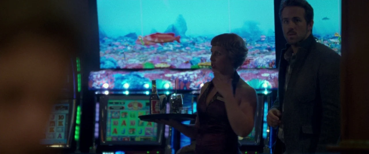 Mississippi Grind (2015) movie still: medium — A woman carrying a serving tray stands in front of a bright digital display. A man stands to her…