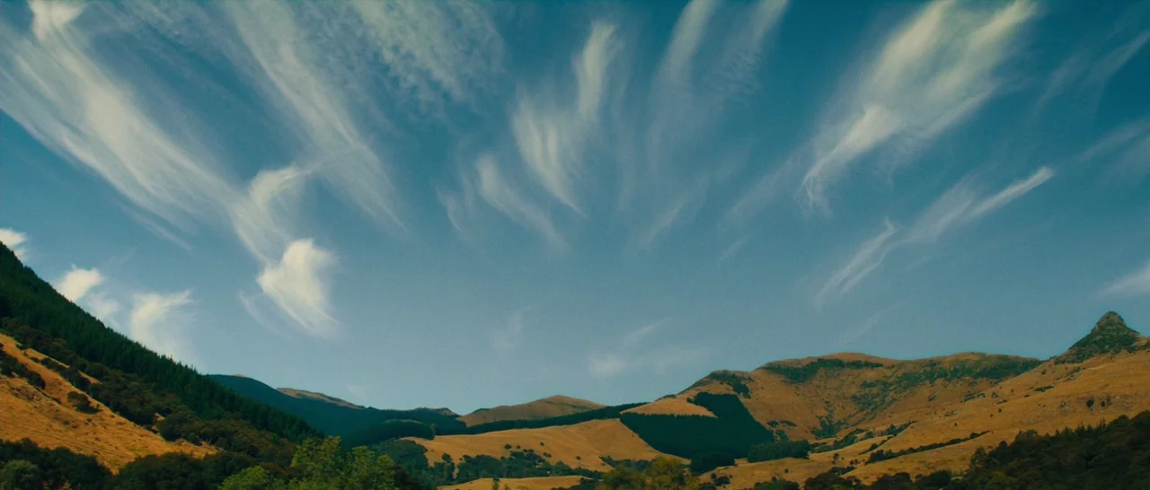 Z for Zachariah (2015) movie still: establishing — A wide mountain range features dry, grassy slopes interspersed with patches of dark pine trees.…