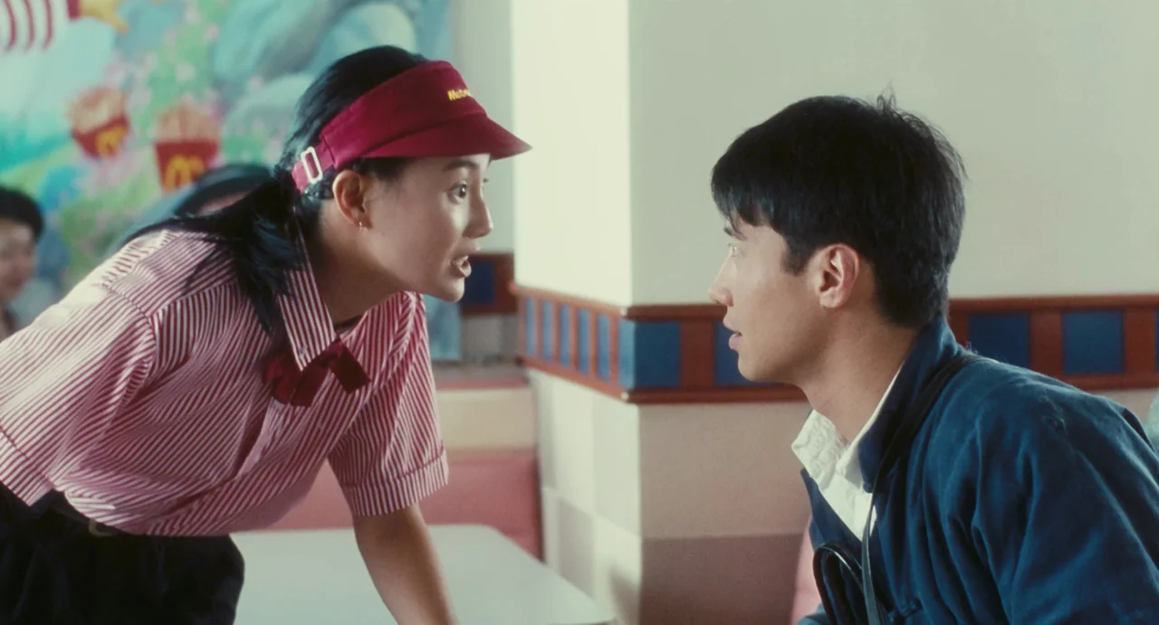 Comrades: Almost A Love Story (1996) movie still: medium — A fast food establishment features retro wall panels and a mural in the background. A…