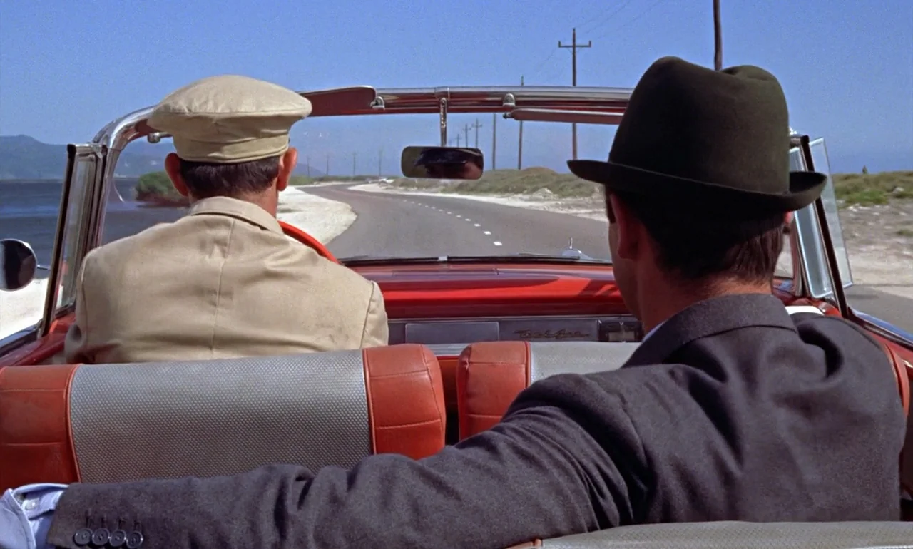 Dr. No (1962) movie still: medium — A coastal road stretches ahead with utility poles lining the horizon under clear skies. Two men sit in a red…