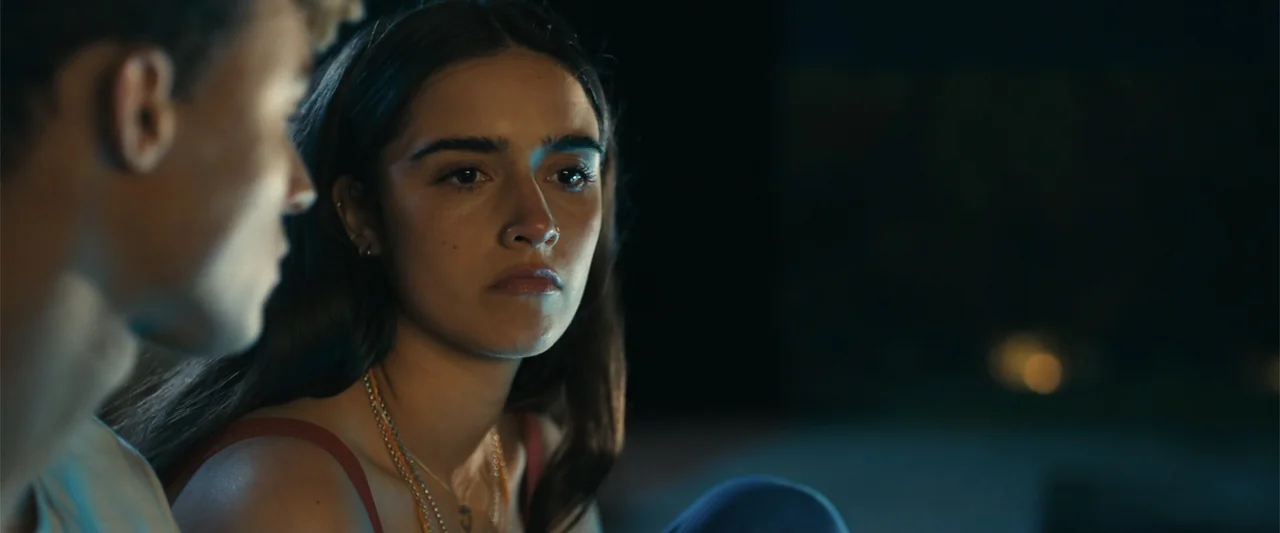 My Fault: London (2025) movie still: closeup — A nighttime setting features a woman in the foreground illuminated by faint blue light. She looks…