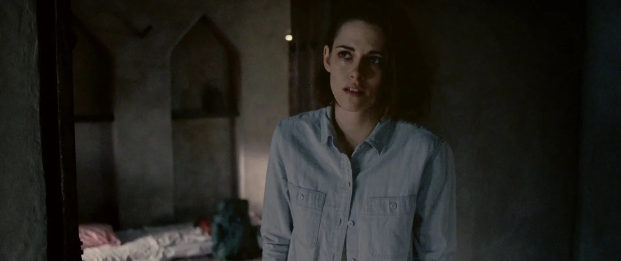 Personal Shopper (2016) movie still: medium — A dimly lit room features two recessed wall arches and a bed with a backpack. A young woman in a blue…