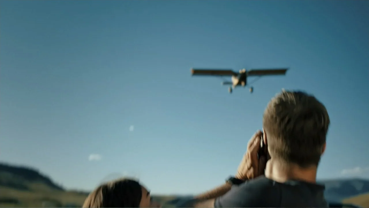 Bullet Proof (2022) movie still: medium — A vast, open outdoor area with rolling hills under a clear blue sky. A man in a t-shirt looks through a…