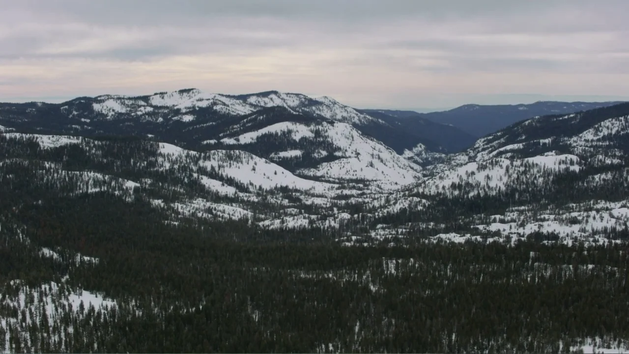 Alex & Emma (2003) movie still: establishing — A vast mountain range covered in snow and pine trees stretches to the horizon. The overcast sky hangs…