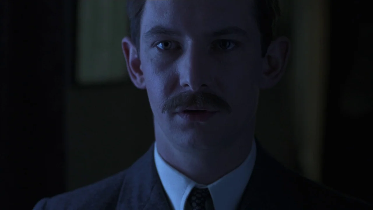 Michael Collins (1996) movie still: closeup — A dark, dimly lit interior space provides a somber setting for a man. A man with a dark mustache…