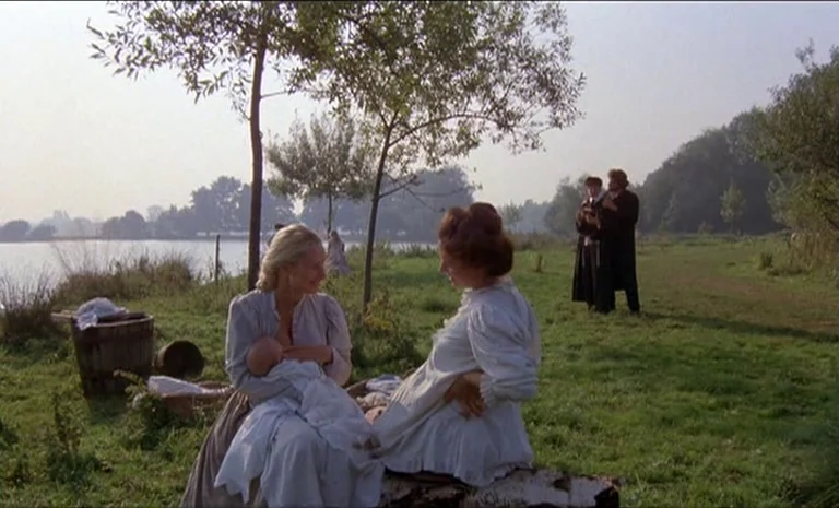 Yentl (1983) movie still: wide — A grassy field beside a lake features two women sitting on a fallen log. Two men stand in the background near a…