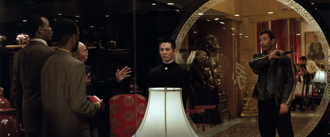 Lethal Weapon 4 (1998) movie still: medium — An upscale interior with dark wood paneling, decorative vases, and a large circular mirror. A man in a…