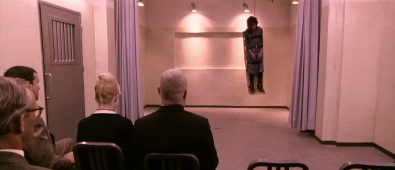 Dancer in the Dark (2000) movie still: wide — A sterile room features a recessed wall alcove containing a person in restraints. Three observers sit…