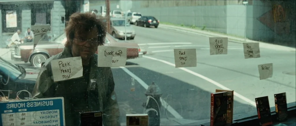 Be Kind Rewind (2008) movie still: medium — A man stands inside a video rental store looking through the front glass window. Several white paper…