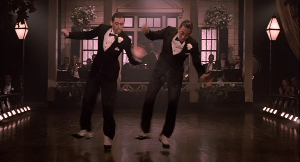 The Cotton Club (1984) movie still: fullbody — A polished wooden stage features two dancers in black tuxedos performing a synchronized routine. In…