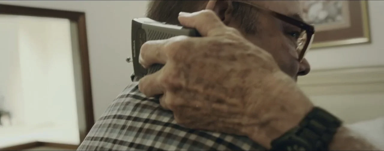 Hunting for Hedonia (2019) movie still: closeup — A bright indoor space with a framed picture on the wall. A hand holds a handheld cassette recorder…