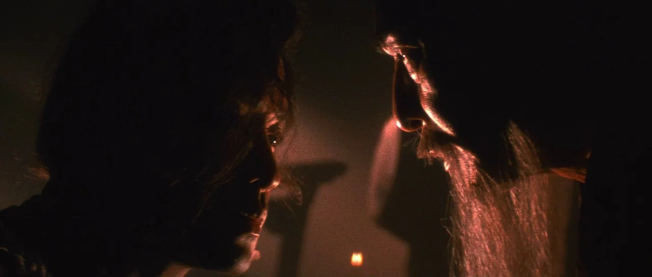 The Bride With White Hair (1993) movie still: closeup — A dark, shadowed chamber is lit by a small, flickering fire source near the floor. A woman…