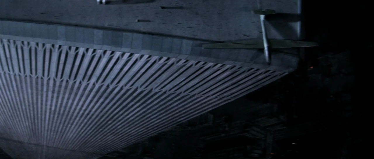 Escape From New York (1981) movie still: establishing — An aerial view of a large, ribbed geometric structure at night. A small aircraft with…