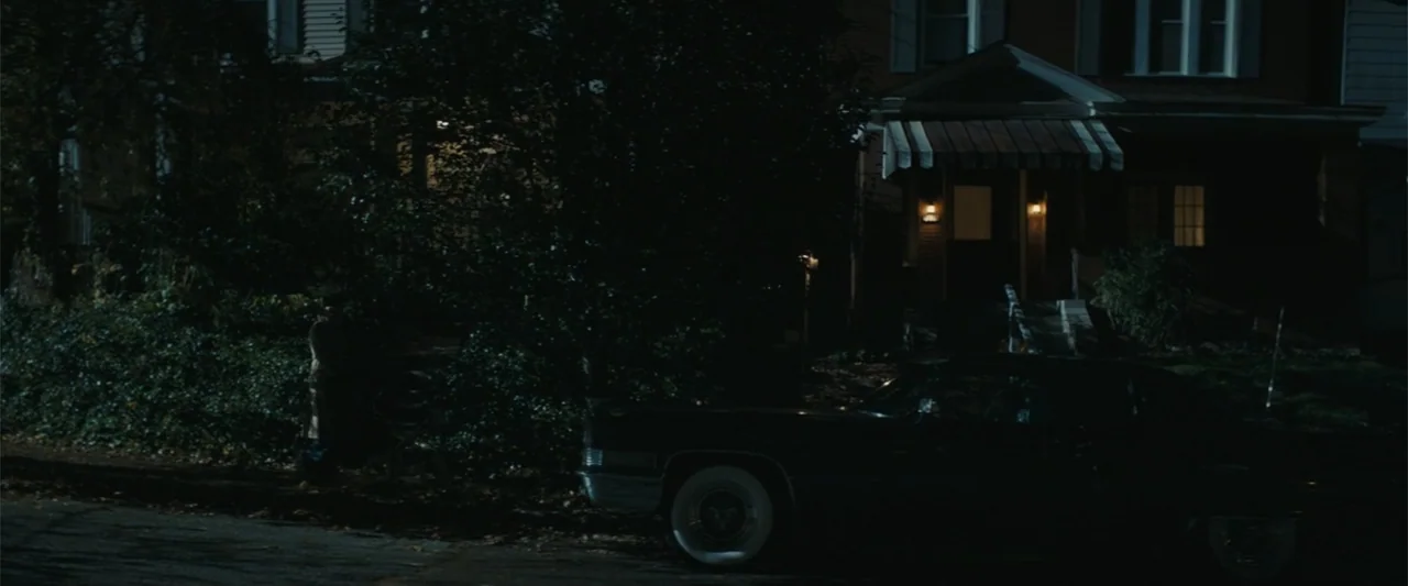 I'm Your Woman (2020) movie still: wide — A dark residential street at night features a large vintage car parked curbside. A traditional two-story…