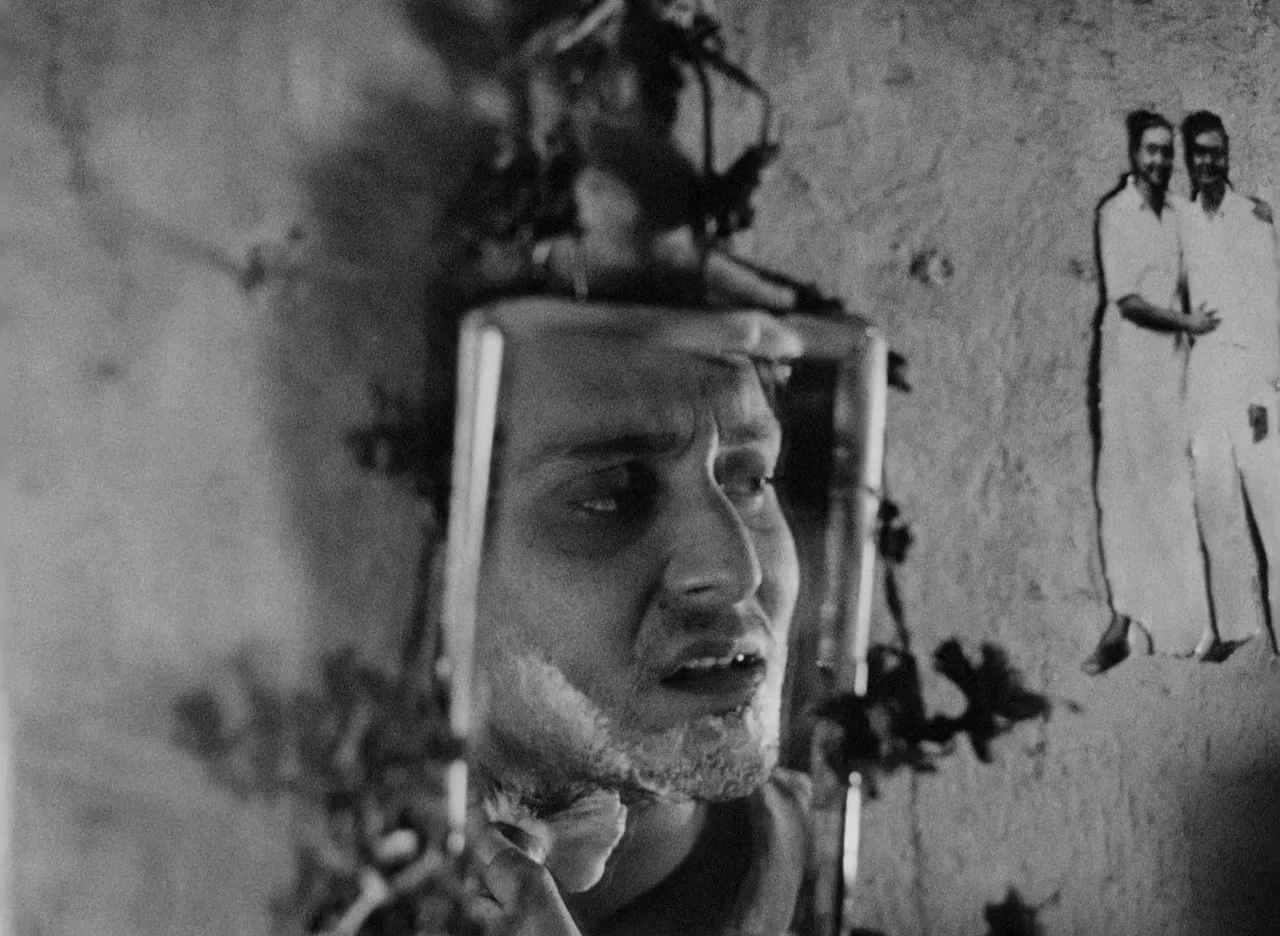 Apur Sansar (1959) movie still: closeup — A man looks into a small handheld mirror in a dark space. A printed photograph of two people stands taped…