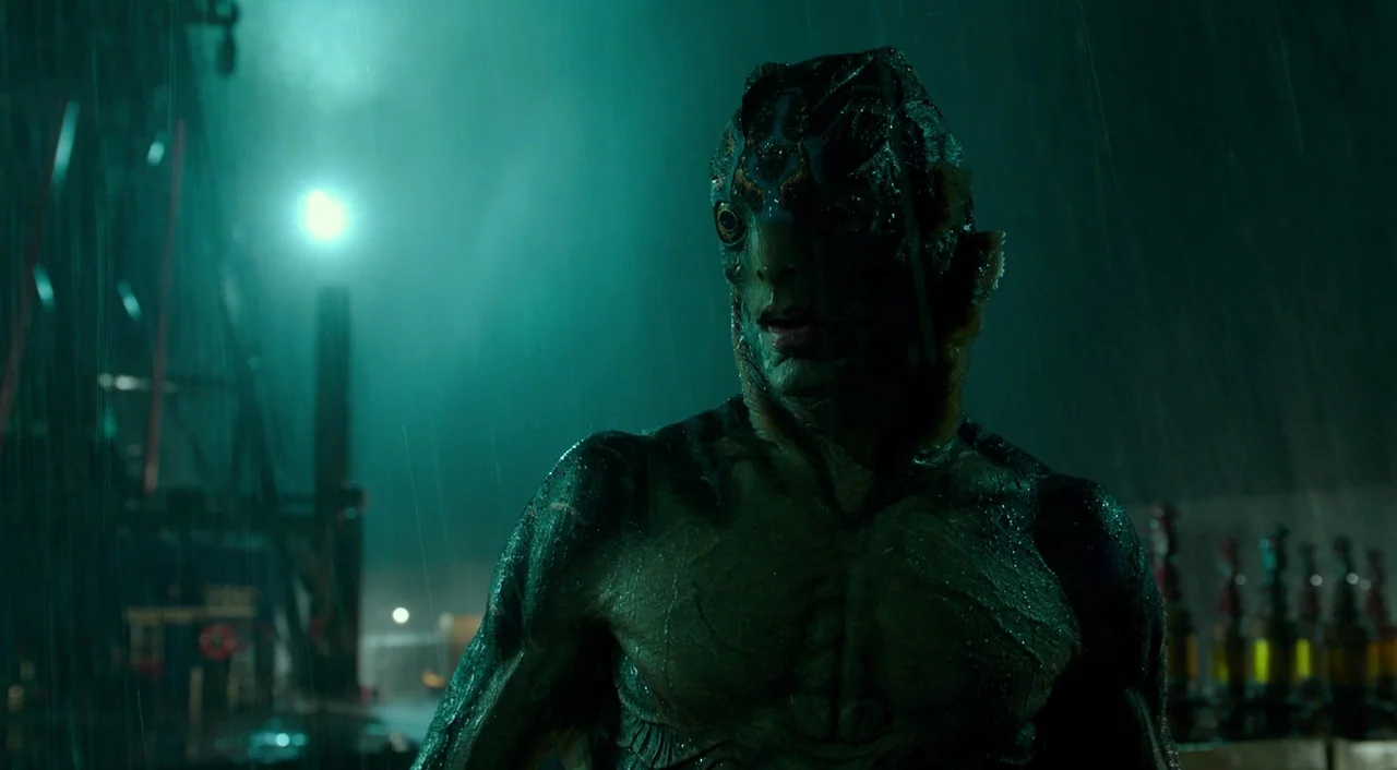 The Shape of Water (2017) movie still: An amphibian creature stands in the pouring rain on a dark, industrial dock, looking cautiously toward…