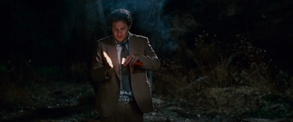 Pineapple Express (2008) movie still: medium — A man stands in a dark outdoor desert environment surrounded by dry brush. He is using a small flame…