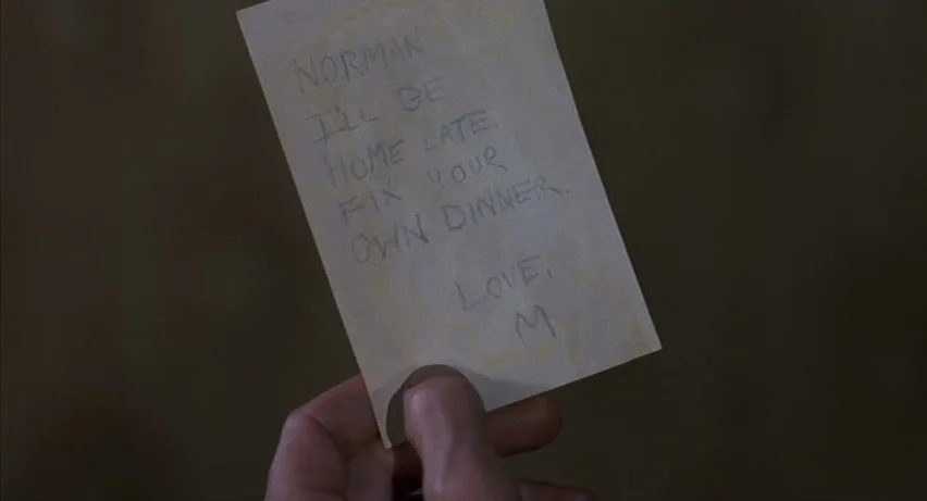 Psycho 2 (1983) movie still: closeup — A close-up view shows a hand holding a rectangular piece of paper. Handwritten text on the note addresses…