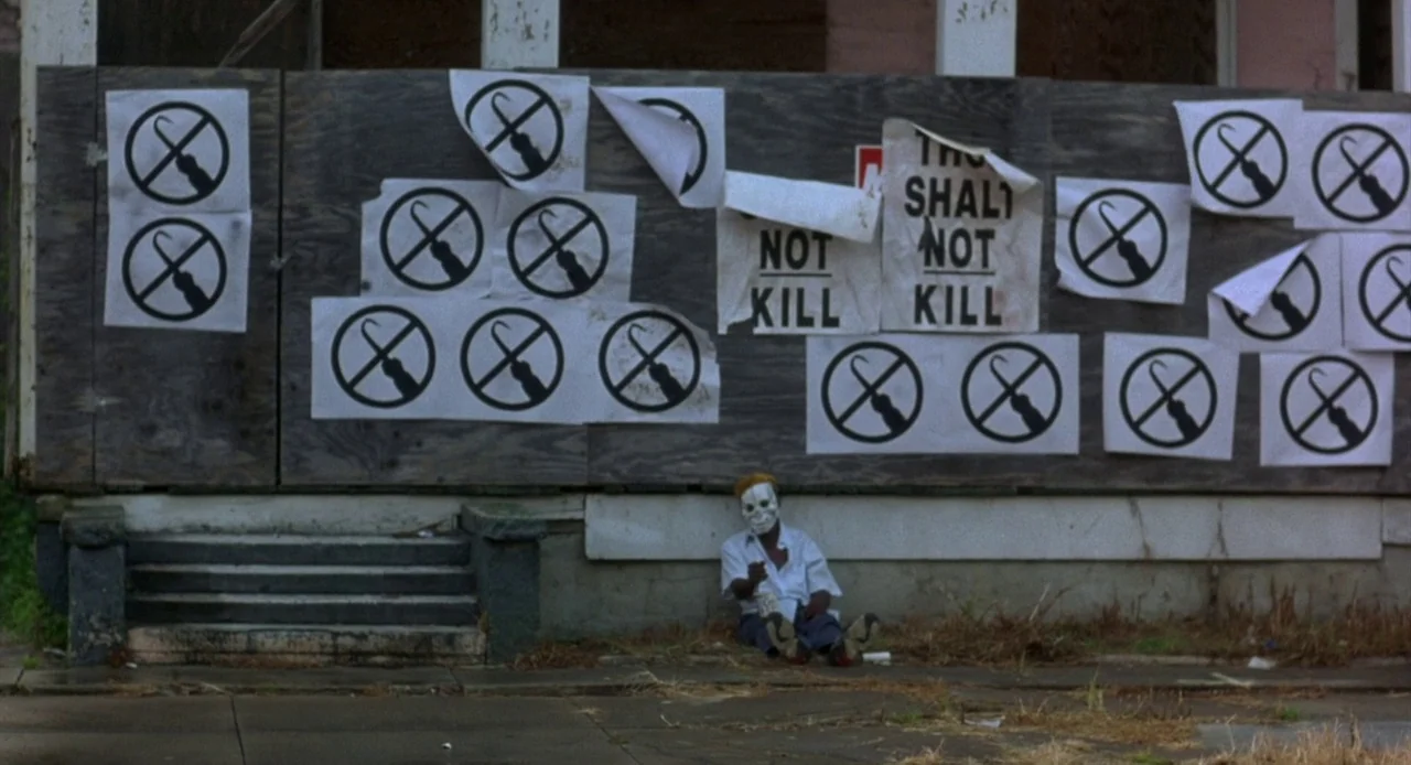 Candyman: Farewell to the Flesh (1995) movie still: wide — A plywood-boarded building facade is covered with multiple white paper protest signs. A…