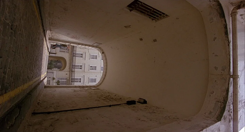 Trainspotting (1996) movie still: establishing — A white-walled arched pedestrian tunnel with a cobblestone ground leads to a street opening. The…
