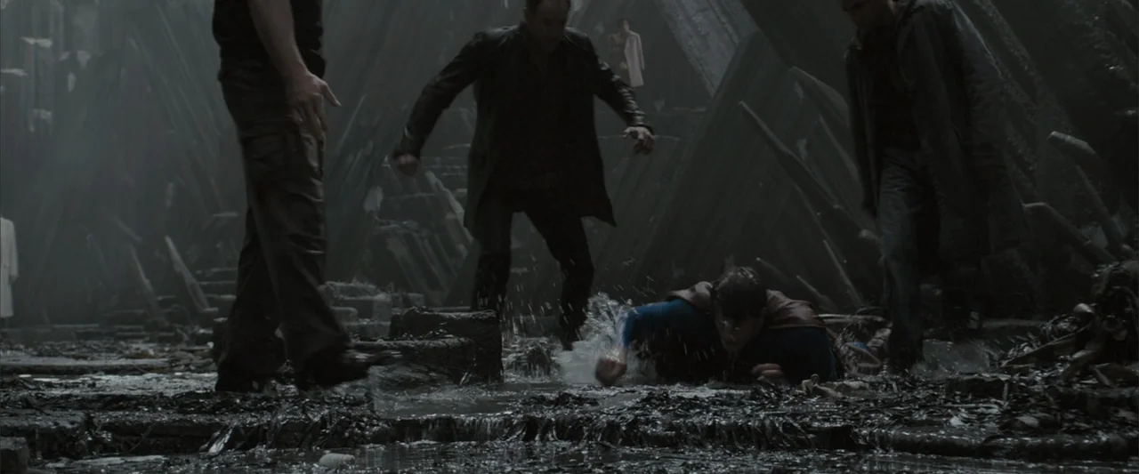 Superman Returns (2006) movie still: medium — A dark, uneven terrain covered in sharp jagged debris and puddles of water. A man wearing a blue suit…