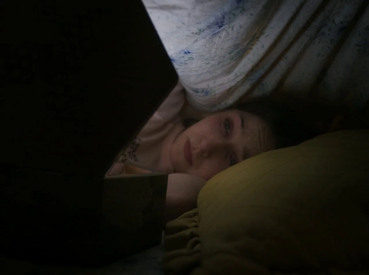 Girl Asleep (2015) movie still: closeup — The interior of a makeshift blanket fort constructed with sheets and pillows. A young woman lies on a…
