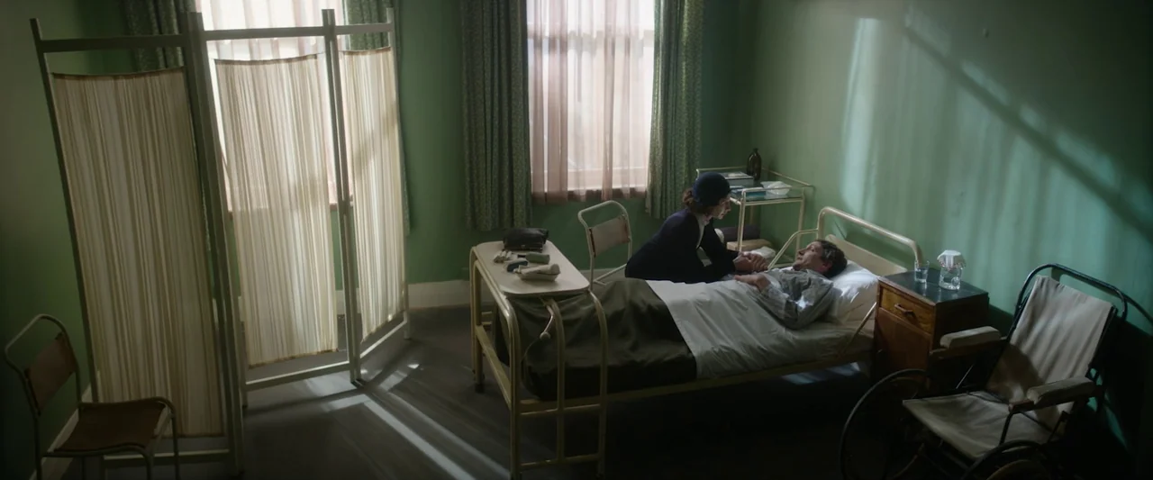 Nandor Fodor and the Talking Mongoose (2023) movie still: wide — A sparsely furnished 1940s medical room has green walls and a single metal bed. A…