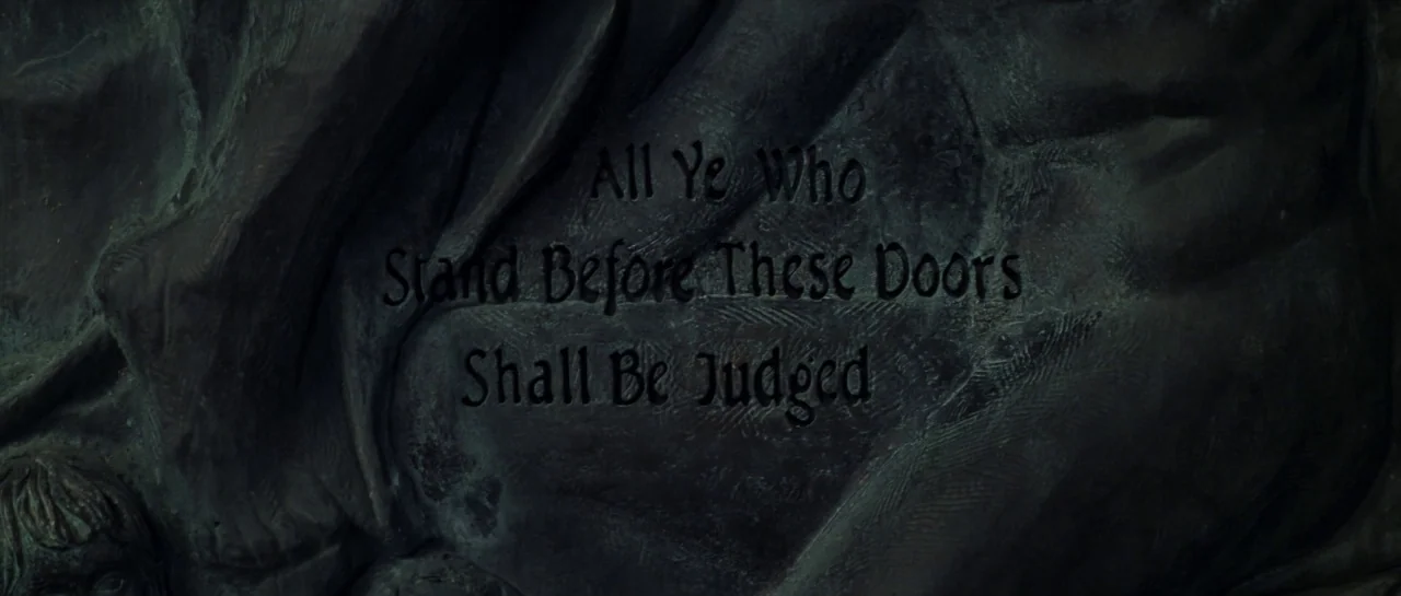 The Haunting (1999) movie still: closeup — A dark, oxidized bronze surface features deeply etched text across a sculptural relief. The inscription…