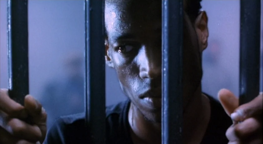 Requiem For A Dream (2000) movie still: closeup — A dark space defined by vertical metal bars blocking the view. A man clutches the bars from behind.