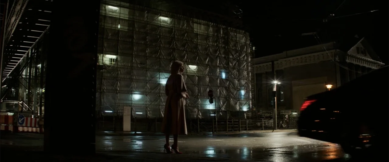 Charlie's Angels (2019) movie still: fullbody — A wet asphalt intersection at night features a large building wrapped in plastic scaffolding. A lone…