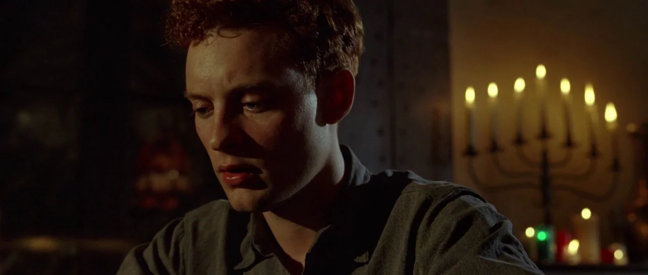 Seabiscuit (2003) movie still: closeup — A dimly lit interior space with dark walls and a burning candelabra nearby. A young man with red hair looks…