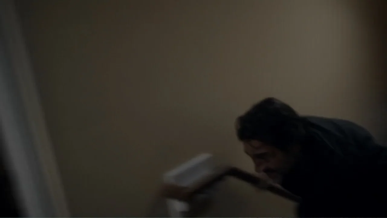 The Messenger (2015) movie still: medium — A dimly lit indoor stairwell features plain walls and a simple wooden handrail. A man moves rapidly down…